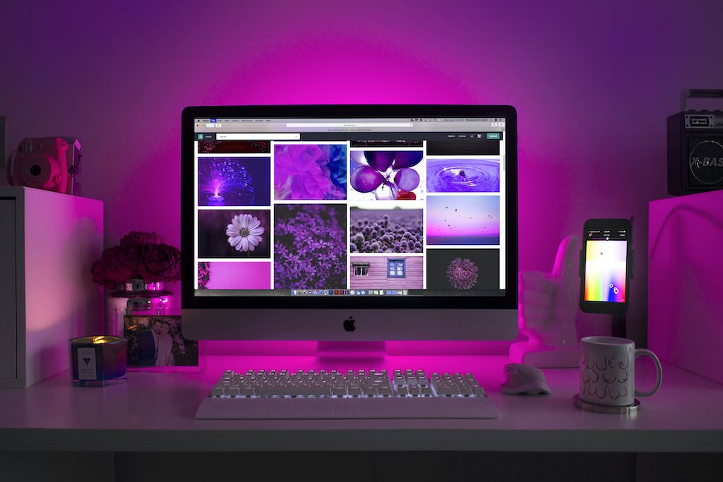 A mac computer showing some website image ideas infront of pink back light